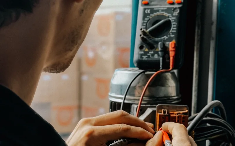 Electrician using a digital multimeter to test terminals while diagnosing an electrical fault
