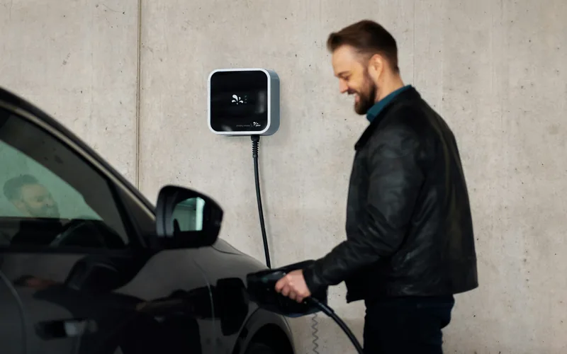 Driver plugging a connector into an electric vehicle beside a wall-mounted Level 2 charger